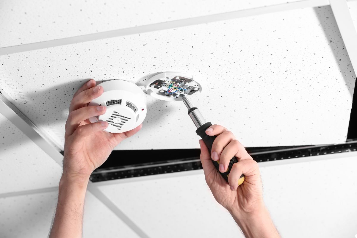 A person using a screwdriver to repair, standing on a ladder with focused concentration. 