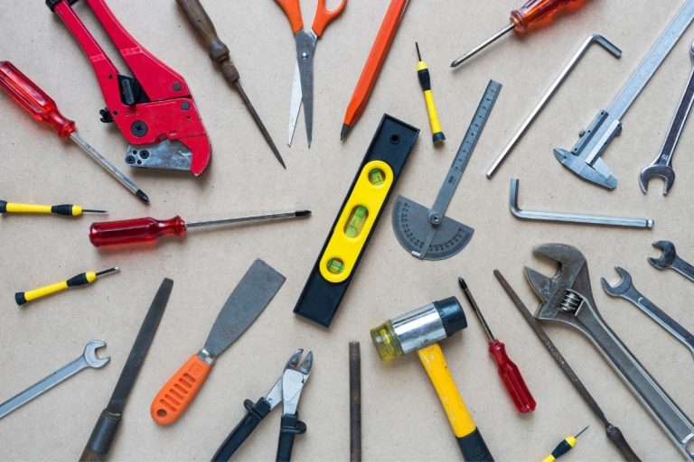 A collection of various tools, such as hammers and drills, arranged methodically on a wooden table surface.